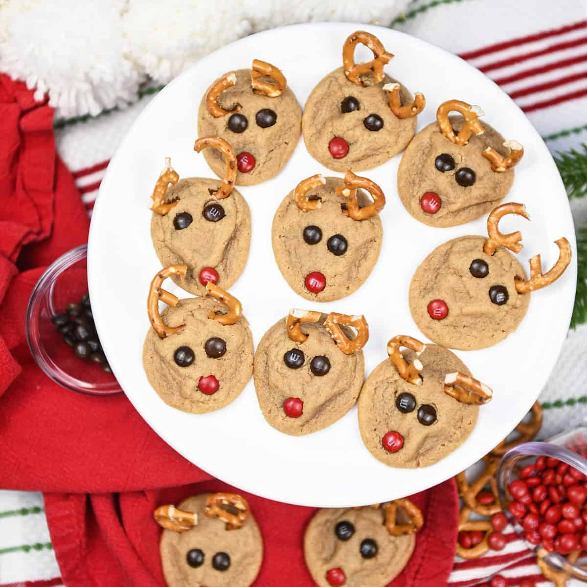 White platter filled with reindeer cookies, each decorated with pretzel antlers and red candy noses.