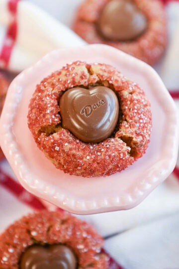 Peanut butter cookie with a chocolate heart center displayed on a pink stand with more cookies surrounding it