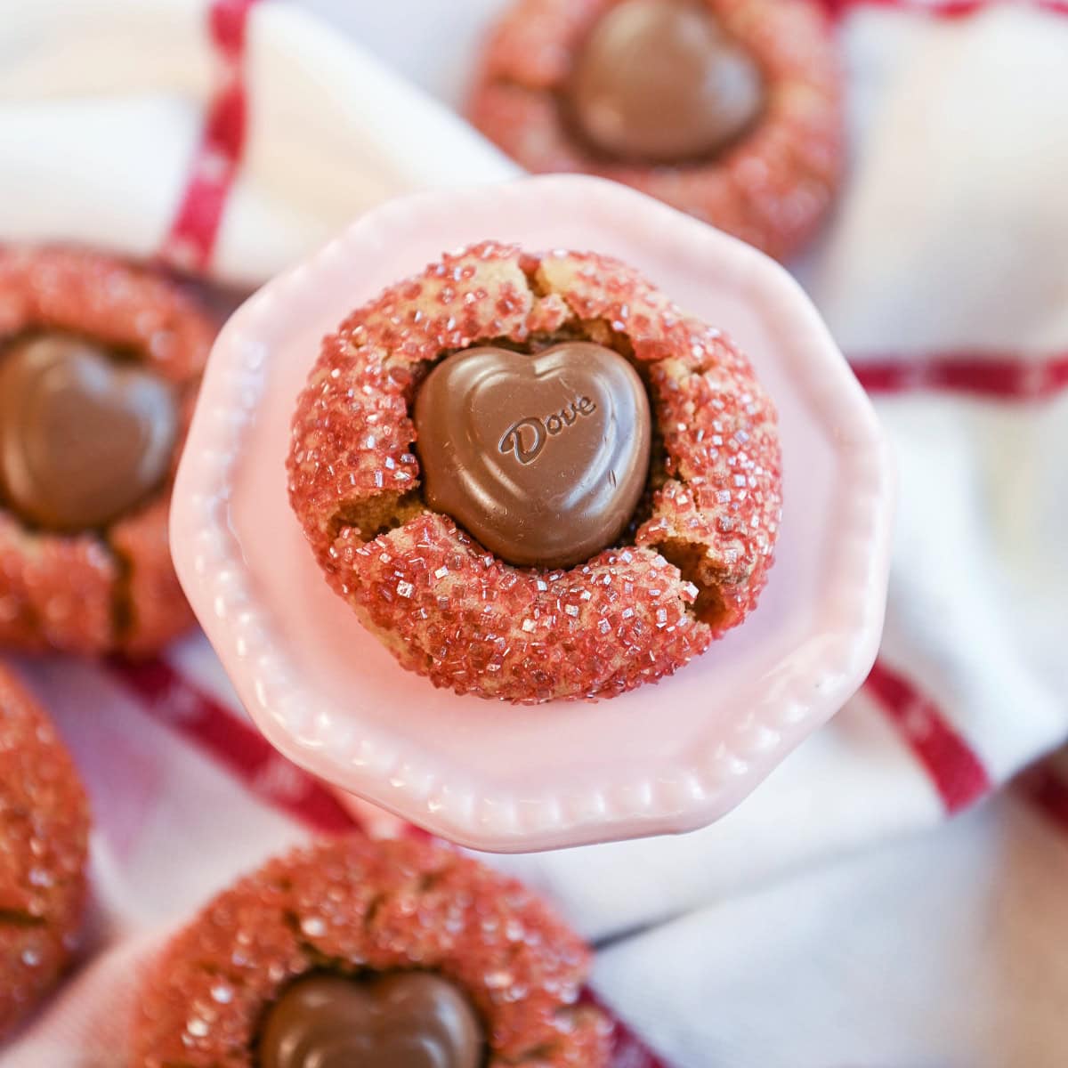 Peanut butter cookie with a chocolate heart center displayed on a pink stand with more cookies surrounding it