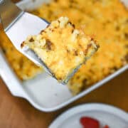 Baked breakfast casserole with sausage, potatoes, eggs, and cheese, served in a white casserole dish.