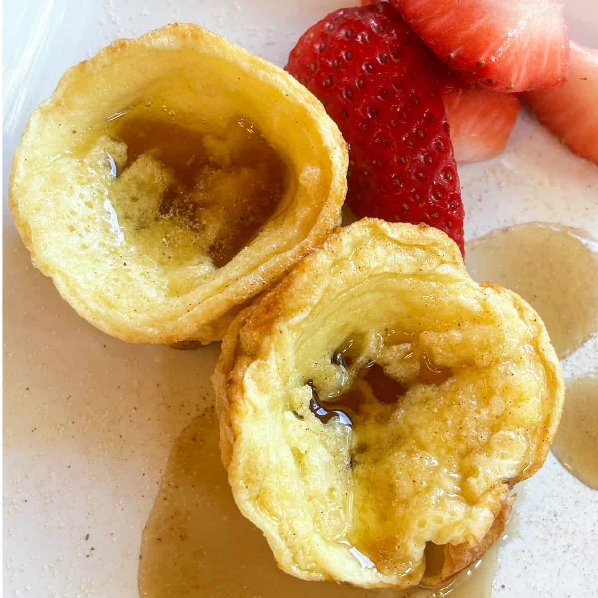 Mini German Pancakes served on a plate, topped with cinnamon sugar and syrup and served with fresh berries.