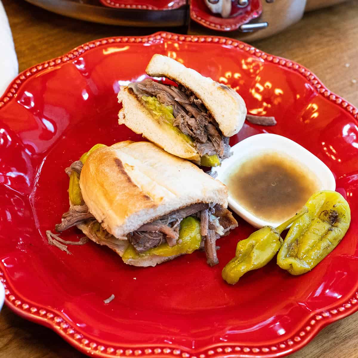 Pepper roast sandwiches piled on hoagie buns and served on a red plate.