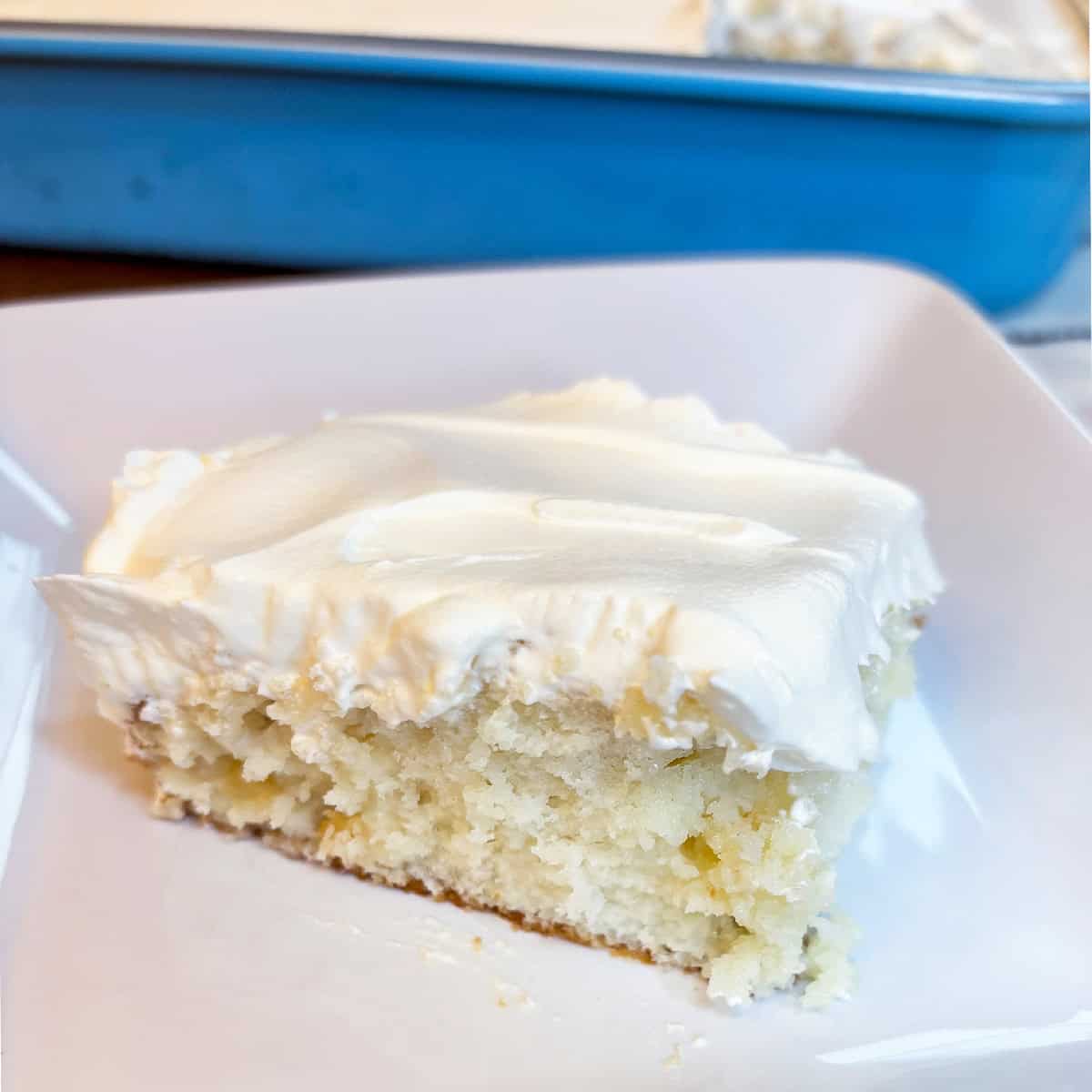 Slice of Piña Colada poke cake topped with whipped cream served on a white plate.