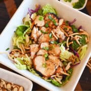 Asian-inspired grilled chicken salad with cabbage, carrots, cucumber, chow mein noodles, and almonds in a white bowl