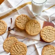 Stack of chewy peanut butter cookies on a plate with a glass of milk in the background.