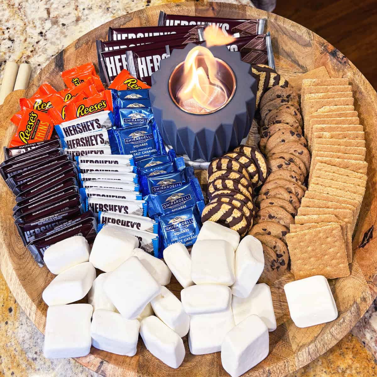 Full overhead shot of an indoor s’mores board with a lit fire pit and assorted sweet treats.