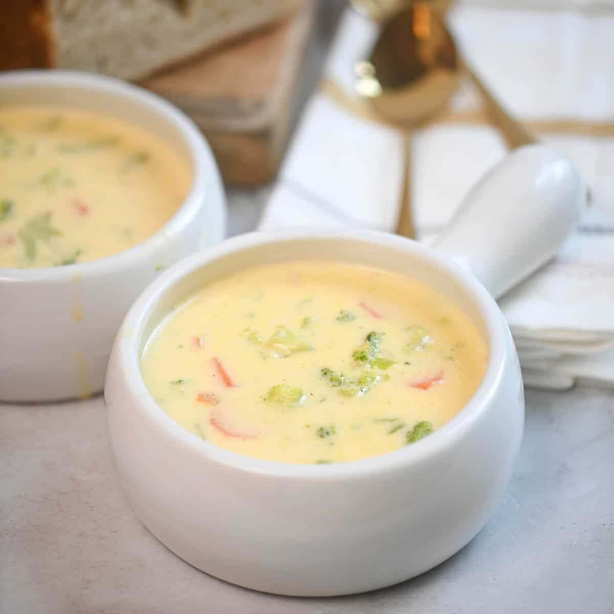 Zoomed-in bowl of broccoli cheddar soup with crusty bread in the background