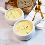 Overhead view of broccoli cheddar soup with chunks of broccoli and bread beside the bowls