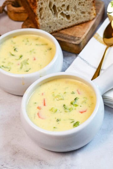 Overhead view of broccoli cheddar soup with chunks of broccoli and bread beside the bowls