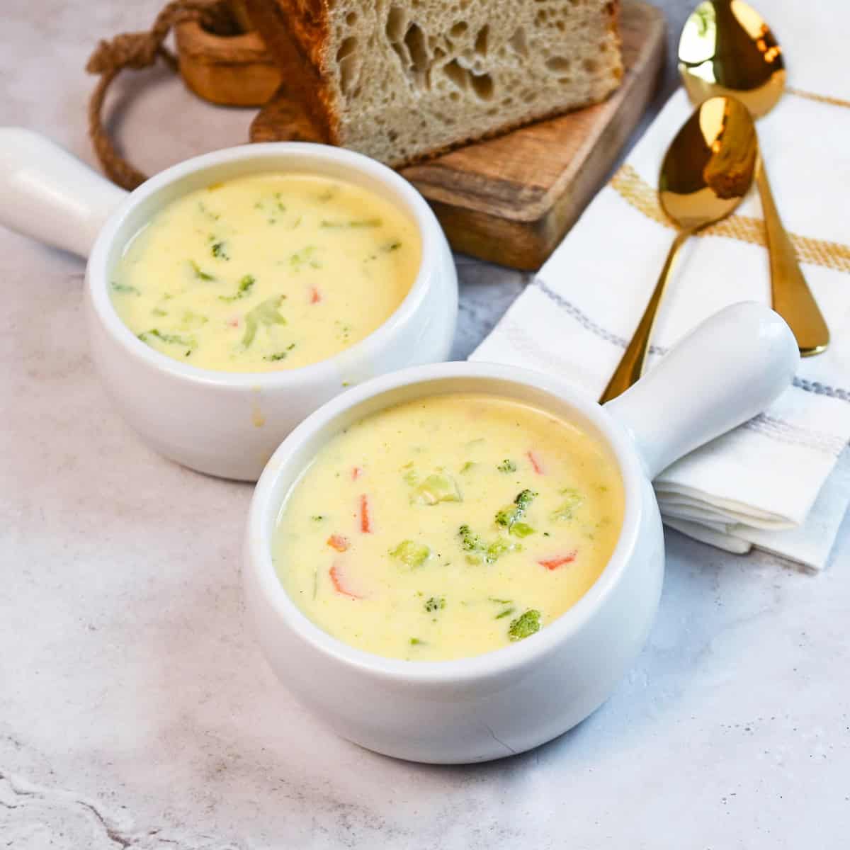 Overhead view of broccoli cheddar soup with chunks of broccoli and bread beside the bowls