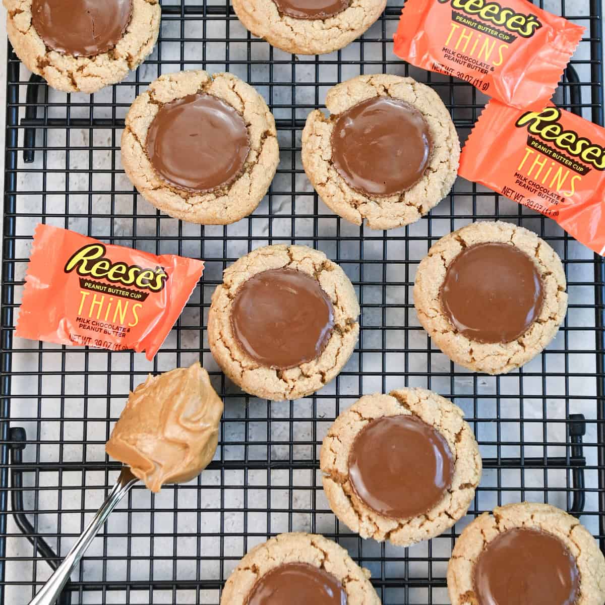 Freshly baked Reese’s Thins Peanut Butter Cookies cooling on a wire rack, with melted chocolate centers.