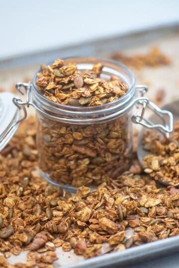 Overhead shot of pumpkin spice granola overflowing in a jar on a wooden surface.
