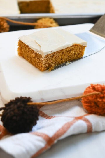 Side view of a slice of pumpkin sheet cake with thick cinnamon cream cheese frosting on a serving spatula.
