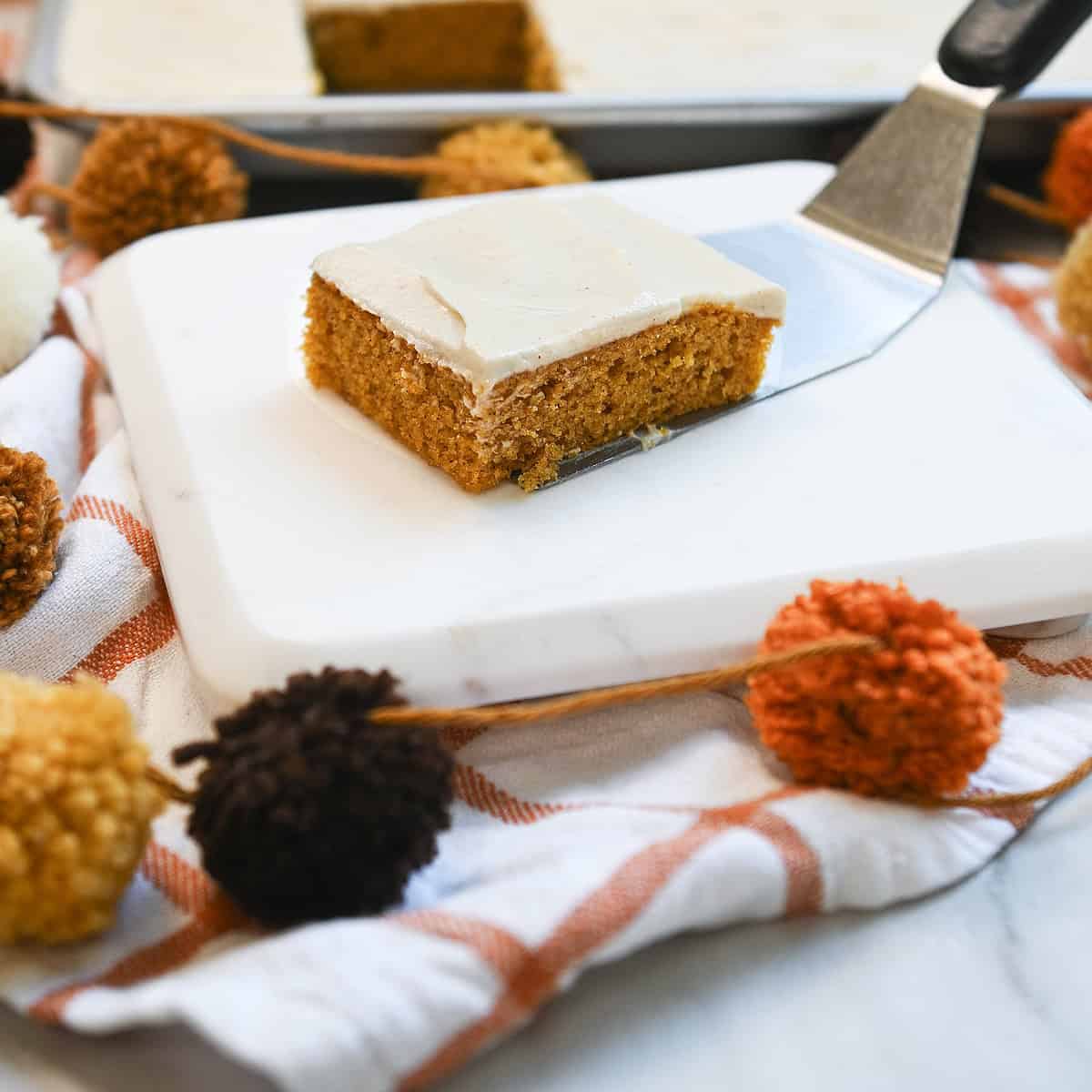 Side view of a slice of pumpkin sheet cake with thick cinnamon cream cheese frosting on a serving spatula.