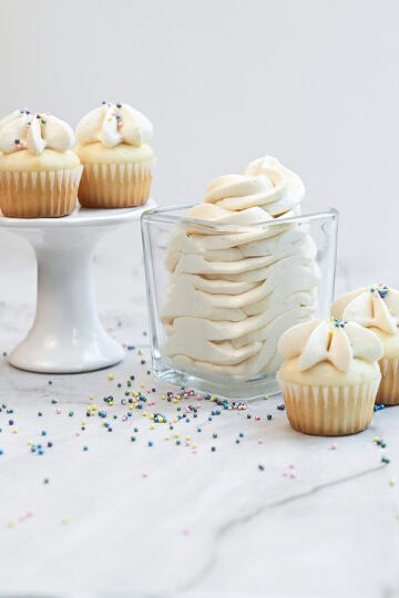 Side view of frosted cupcakes with sprinkles next to a jar of vanilla buttercream.