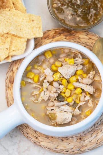 Close-up of chicken chile soup in a bowl with tortilla chips and cheese on the side.