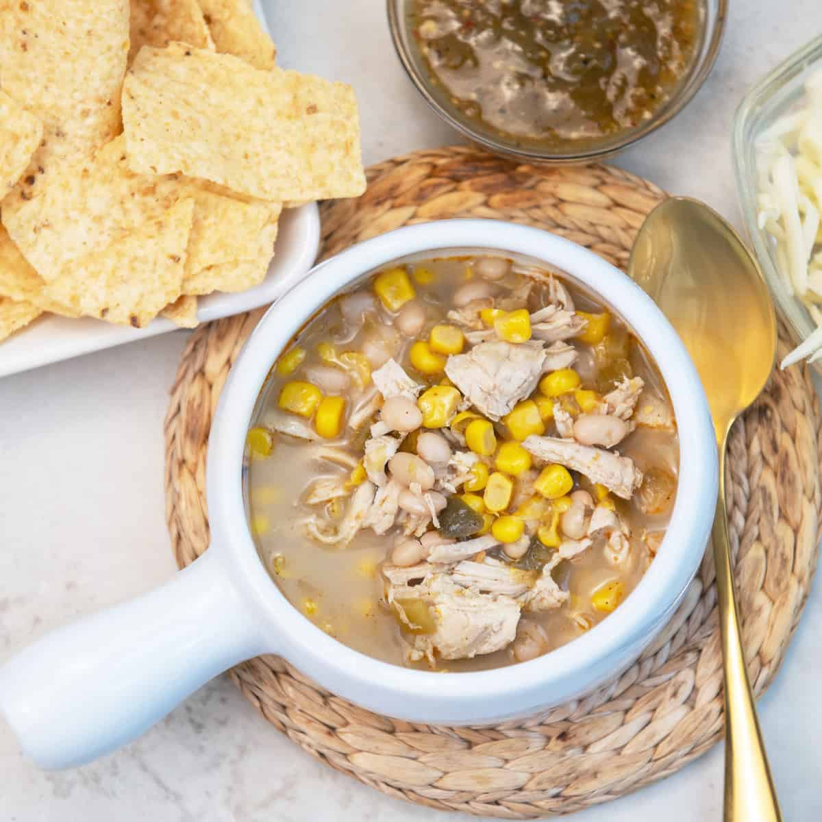 Close-up of chicken chile soup in a bowl with tortilla chips and cheese on the side.
