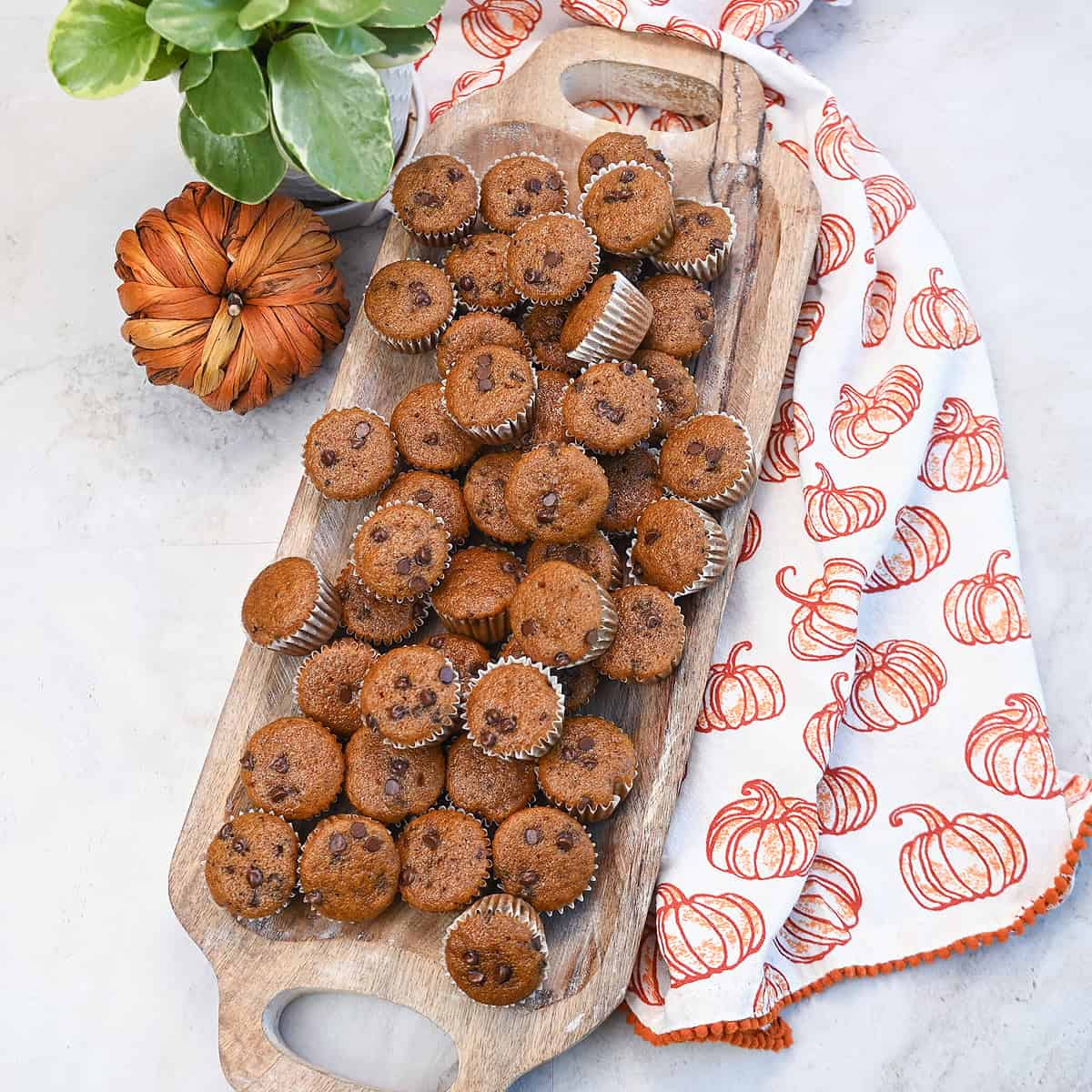 Mini pumpkin chocolate chip muffins arranged neatly on a wooden tray.