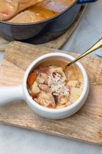 Bowl of Cajun sausage and bean soup with a spoon inside, topped with grated parmesan cheese.
