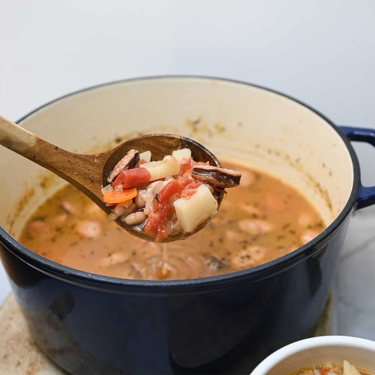 A ladle filled with Cajun sausage and bean soup with chunks of sausage, beans, potatoes, and carrots.