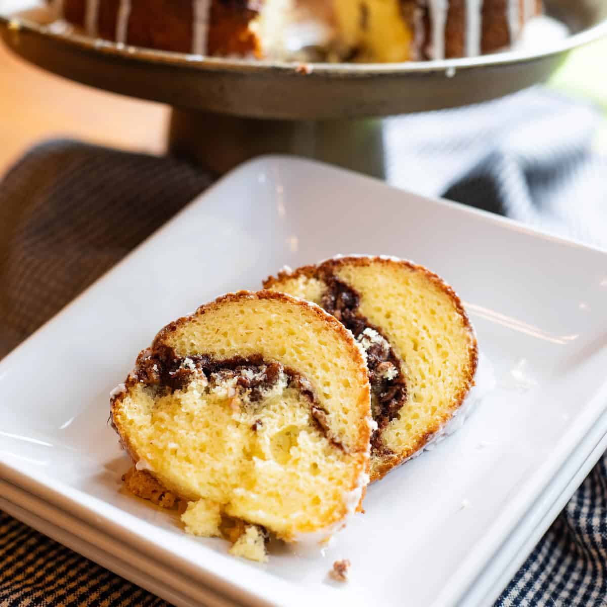 Slice of Sock It to Me cake with cinnamon-pecan swirl on a white plate, whole cake in the background.