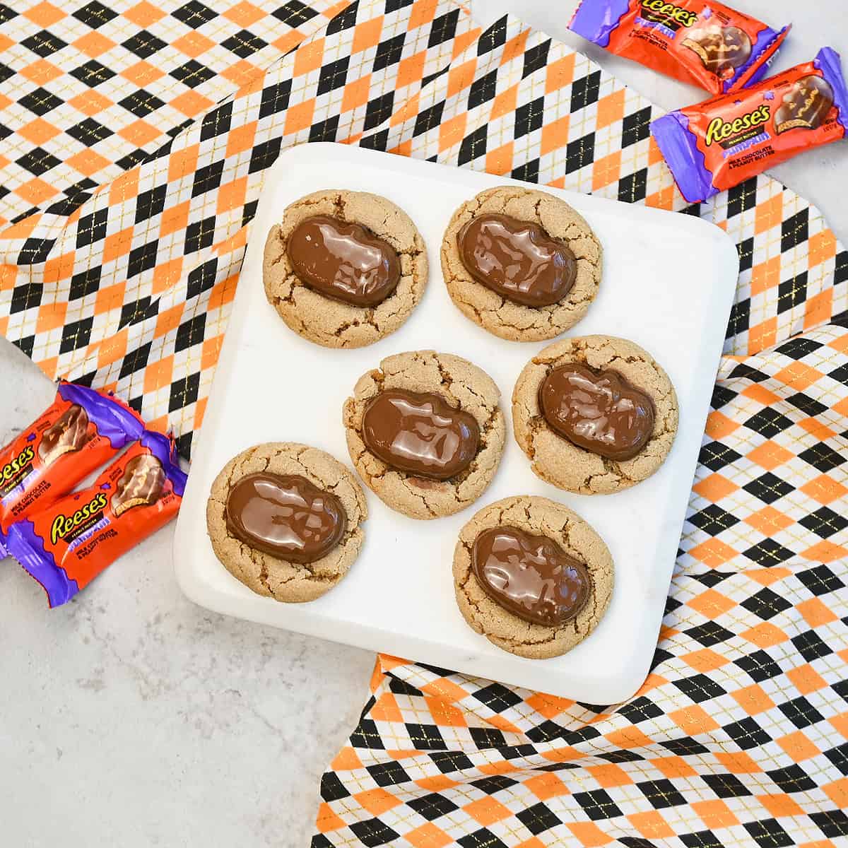 Halloween Reeses peanut butter cookies topped with Reese’s pumpkins arranged on a white platter surrounded by festive Halloween decor.