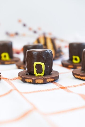 Chocolate marshmallow Pilgrim hats in front of a colorful and festive Thanksgiving backdrop.