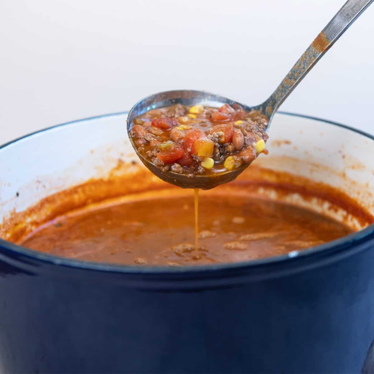 A large pot of hearty taco soup filled with ground beef, beans, and corn, with a ladle lifting a scoop of the flavorful soup.