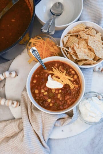 Bowls of taco soup topped with shredded cheese, sour cream, and tortilla chips for a hearty and flavorful meal.