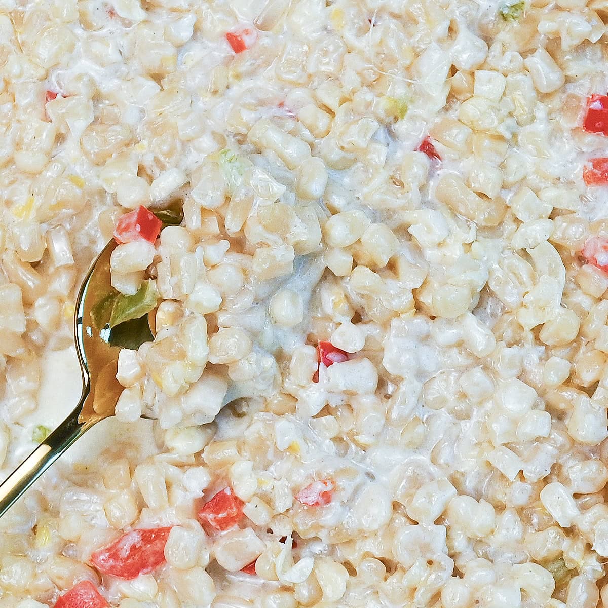 Close-up of creamy White Corn Casserole with red and green peppers and a serving spoon scooping out a portion.