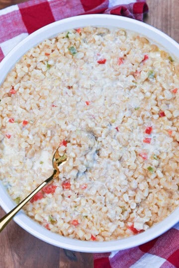 White Corn Casserole in a white baking dish with a red and white towel beside it, showing the creamy corn and peppers.