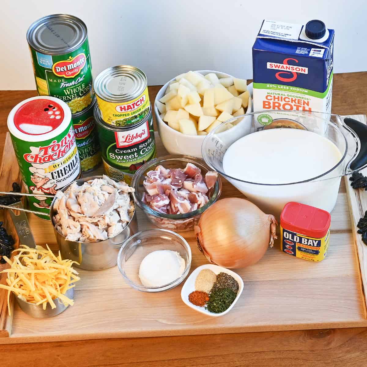 Ingredients for chicken corn chowder including chicken, potatoes, corn, green chiles, bacon, cheese, and seasonings on a kitchen counter.