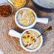 Two white bowls filled with creamy chicken corn chowder topped with bacon and cheese.