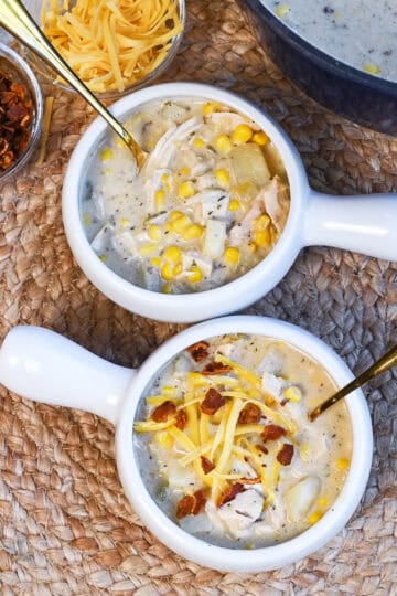 Two white bowls filled with creamy chicken corn chowder topped with bacon and cheese.