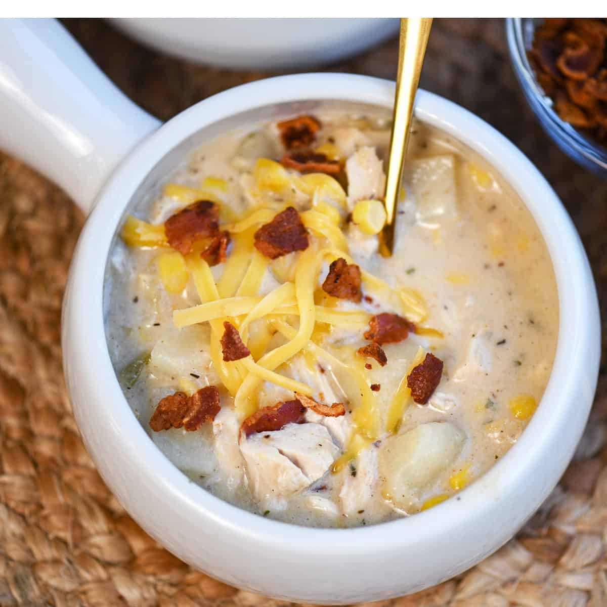 Close-up of chicken corn chowder topped with crispy bacon and melted cheese in a white bowl.