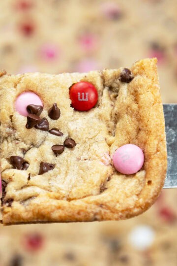 Close-up of a chewy corner piece of Valentine M&M Cookie Bars loaded with chocolate chips and M&M candies.
