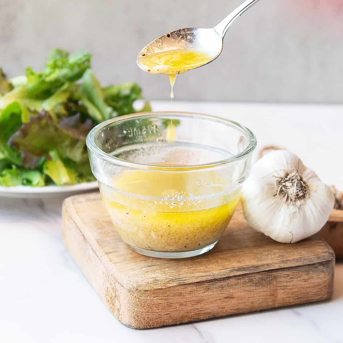 Spoon lifting vinaigrette as dressing drizzles back into the bowl in a smooth stream.