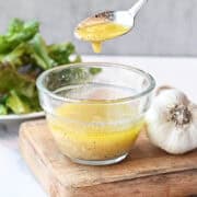 Close-up of vinaigrette dripping from a spoon into the bowl, highlighting its glossy texture.