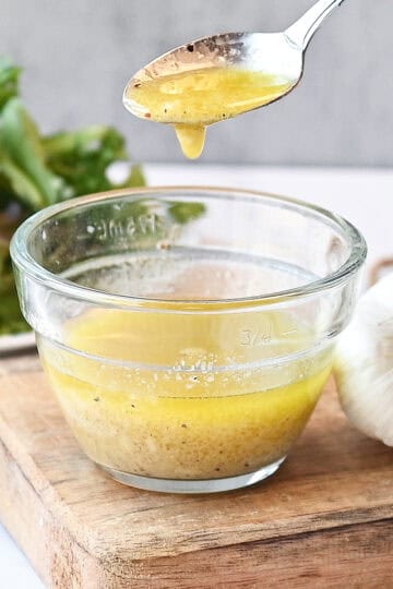 Close-up of vinaigrette dripping from a spoon into the bowl, highlighting its glossy texture.