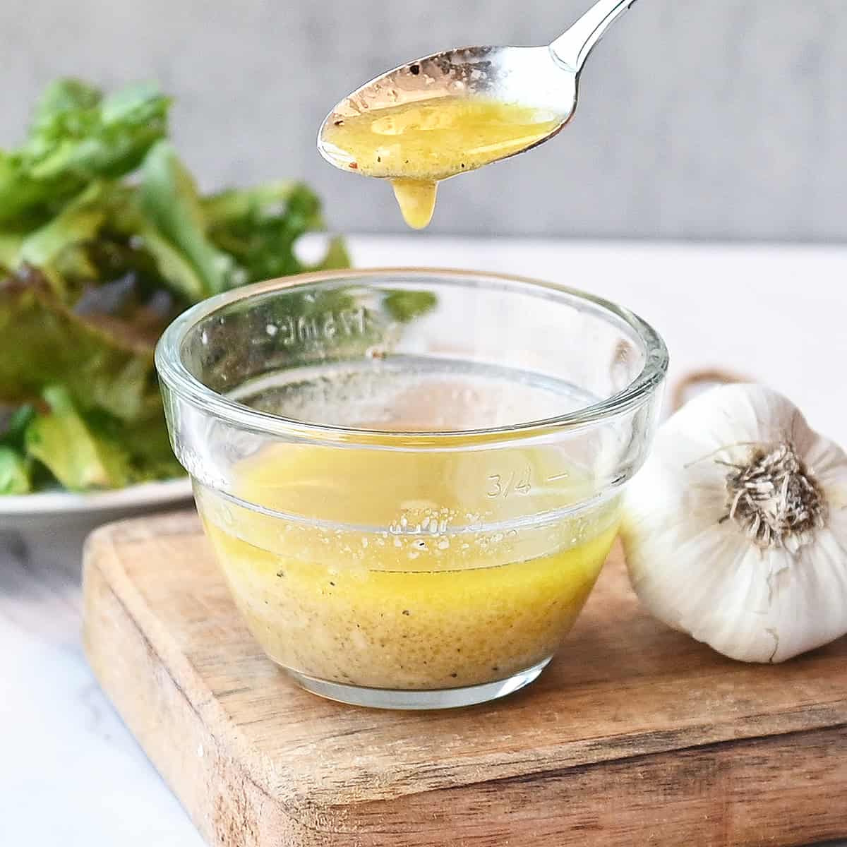 Close-up of vinaigrette dripping from a spoon into the bowl, highlighting its glossy texture.