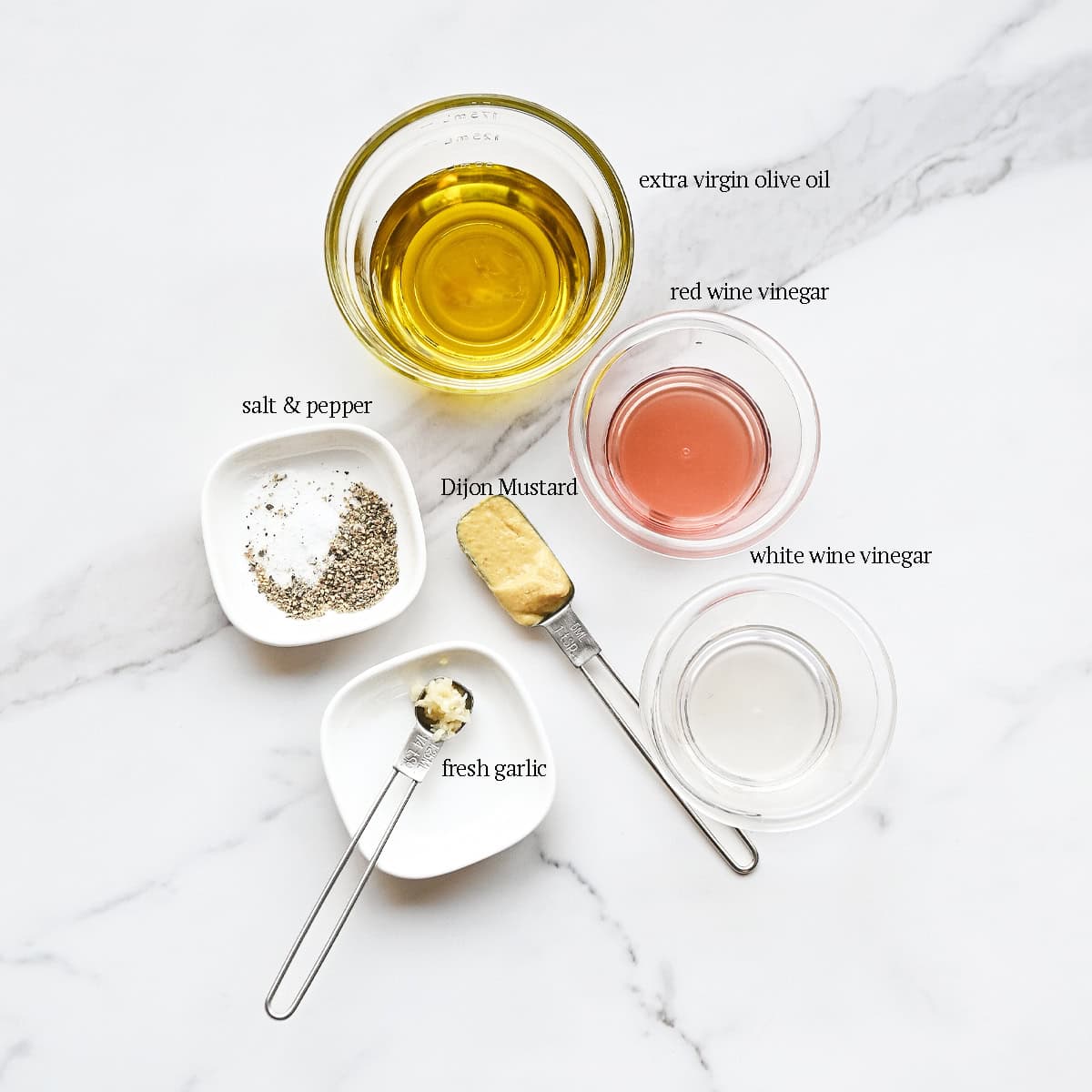 Ingredients for simple vinaigrette labeled on a countertop including olive oil, red wine vinegar, white wine vinegar, Dijon mustard, and seasonings.