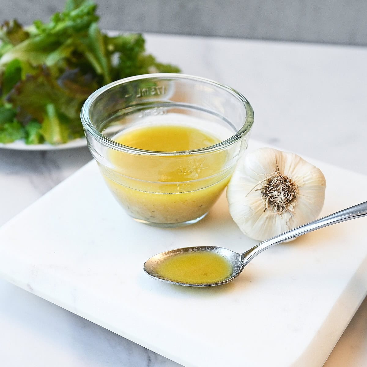 Spoonful of vinaigrette held above a bowl with visible black pepper and seasonings throughout the dressing.