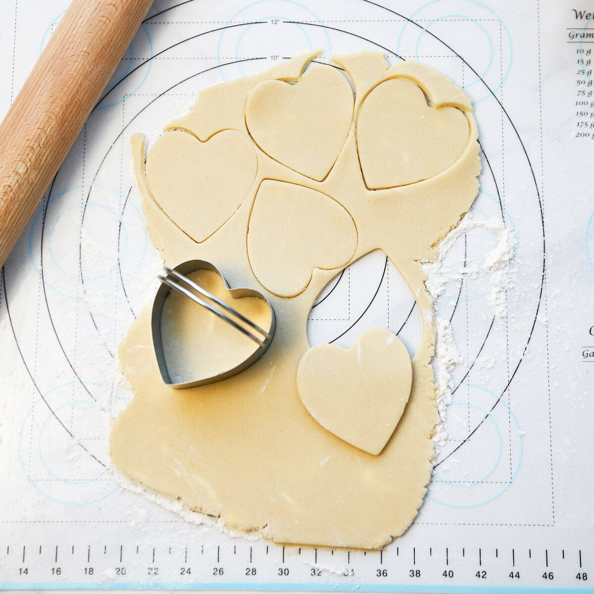 Valentine sugar cookies being cut from rolled dough using heart-shaped cookie cutters.