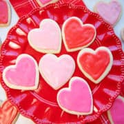 Decorated Valentine sugar cookies with pink and red icing arranged on a red plate.