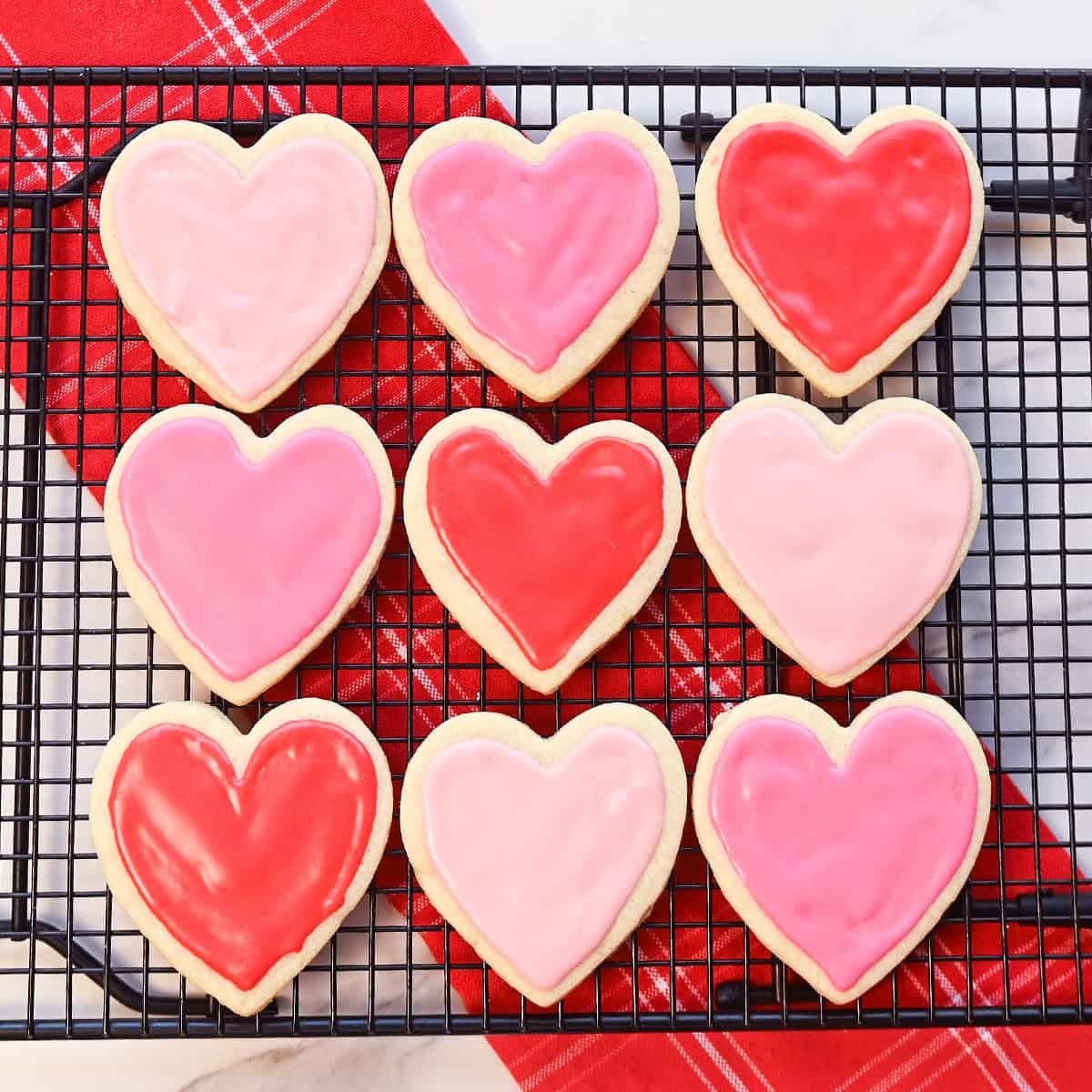 Valentine sugar cookies decorated with pink and red icing cooling on a black wire rack.