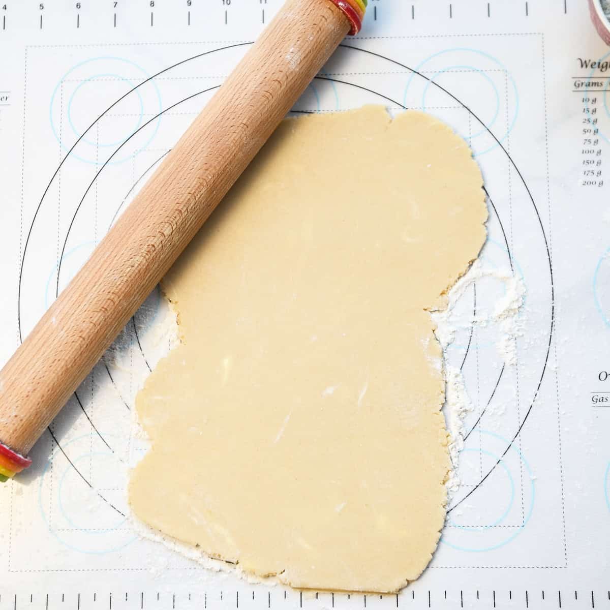 Sugar cookie dough rolled out on a floured surface with a rolling pin ready for cutting.
