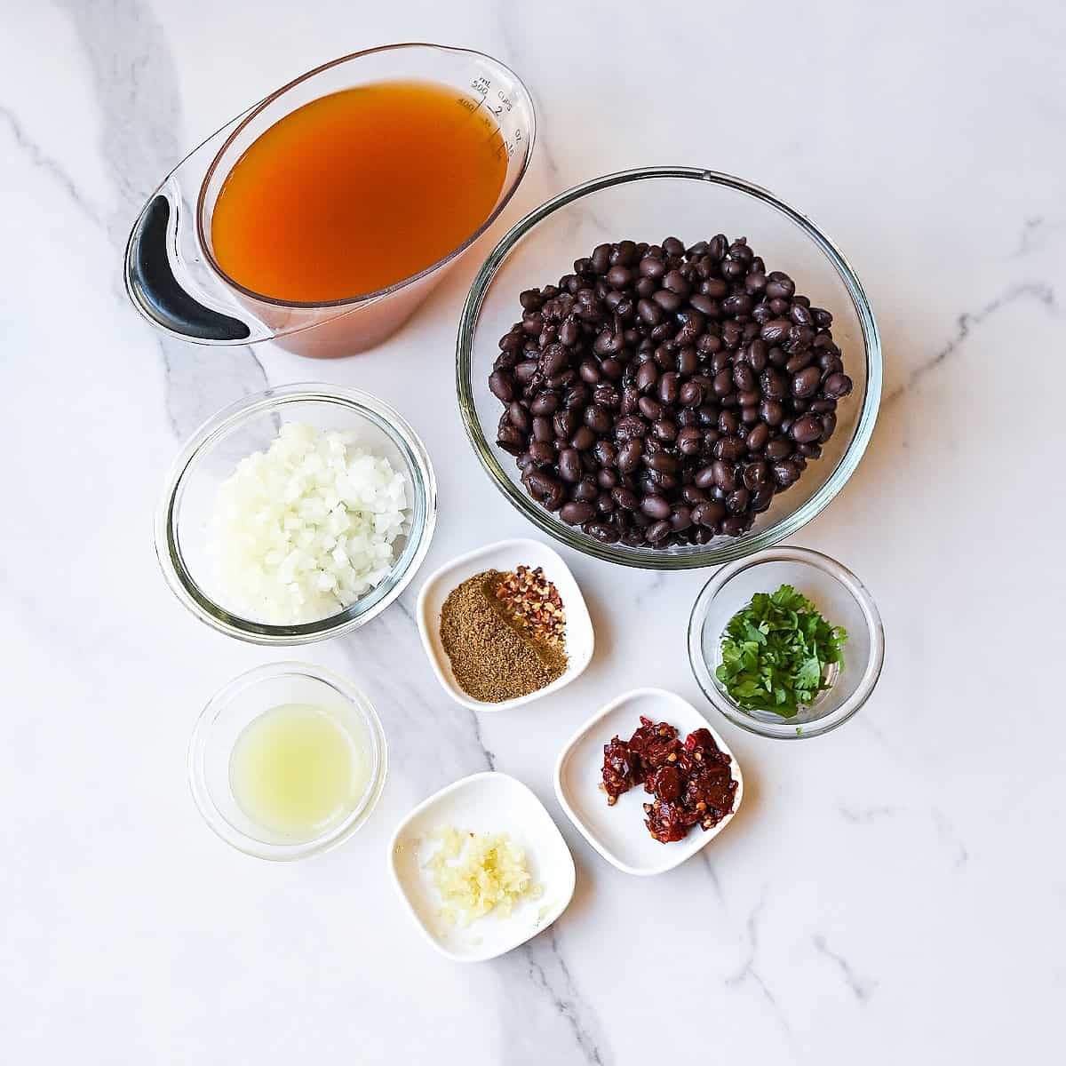 Ingredients for easy black bean soup including black beans, onion, garlic, broth, spices, and fresh cilantro arranged on a kitchen counter.