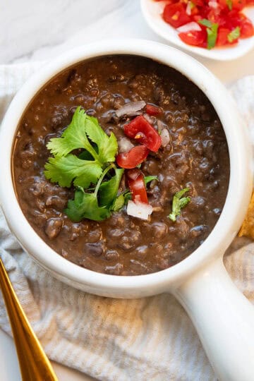 Close overhead view of thick black bean soup garnished with pico de gallo and cilantro in a white bowl with tortilla chips.