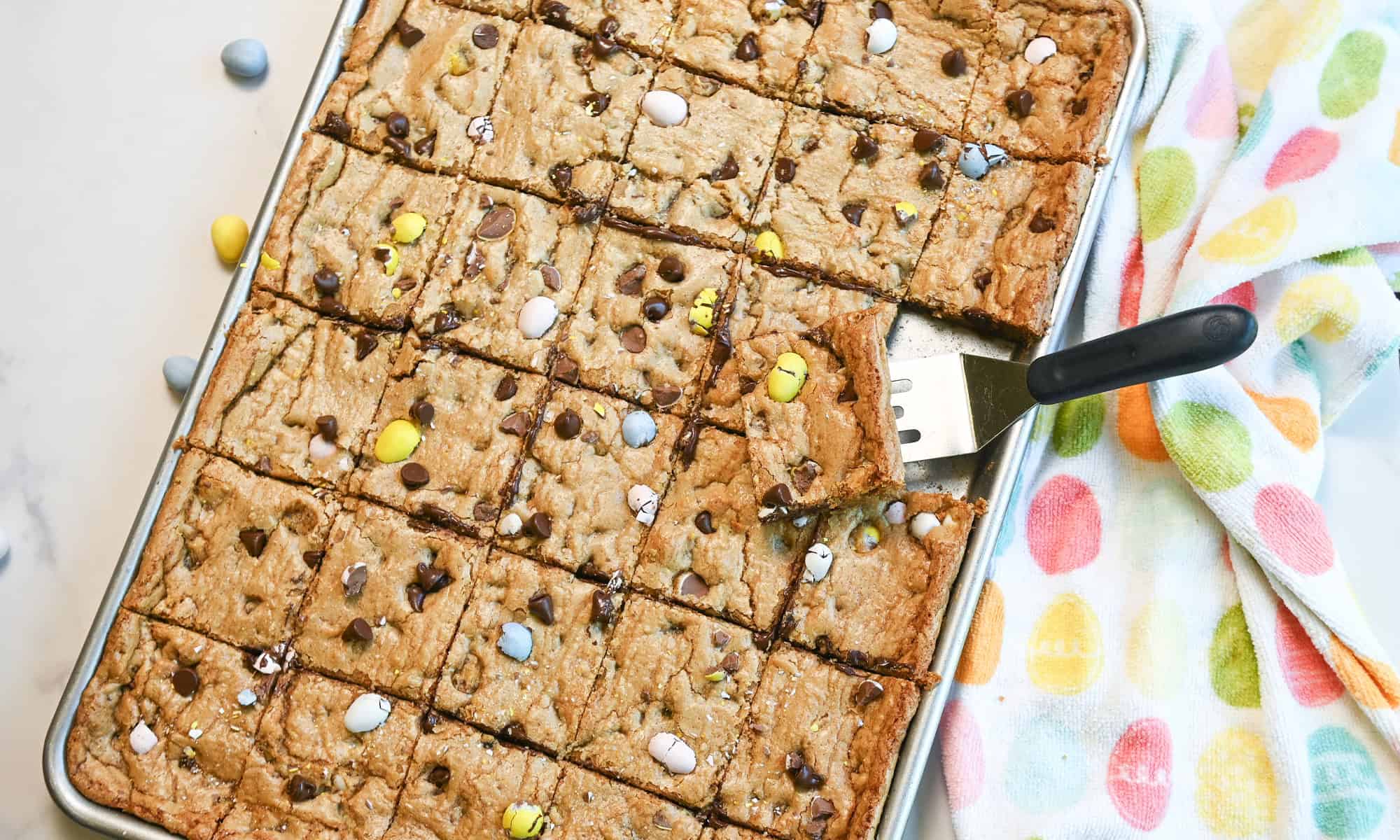 Cadbury Egg cookie bars arranged for serving with visible chocolate chips and colorful candy pieces.