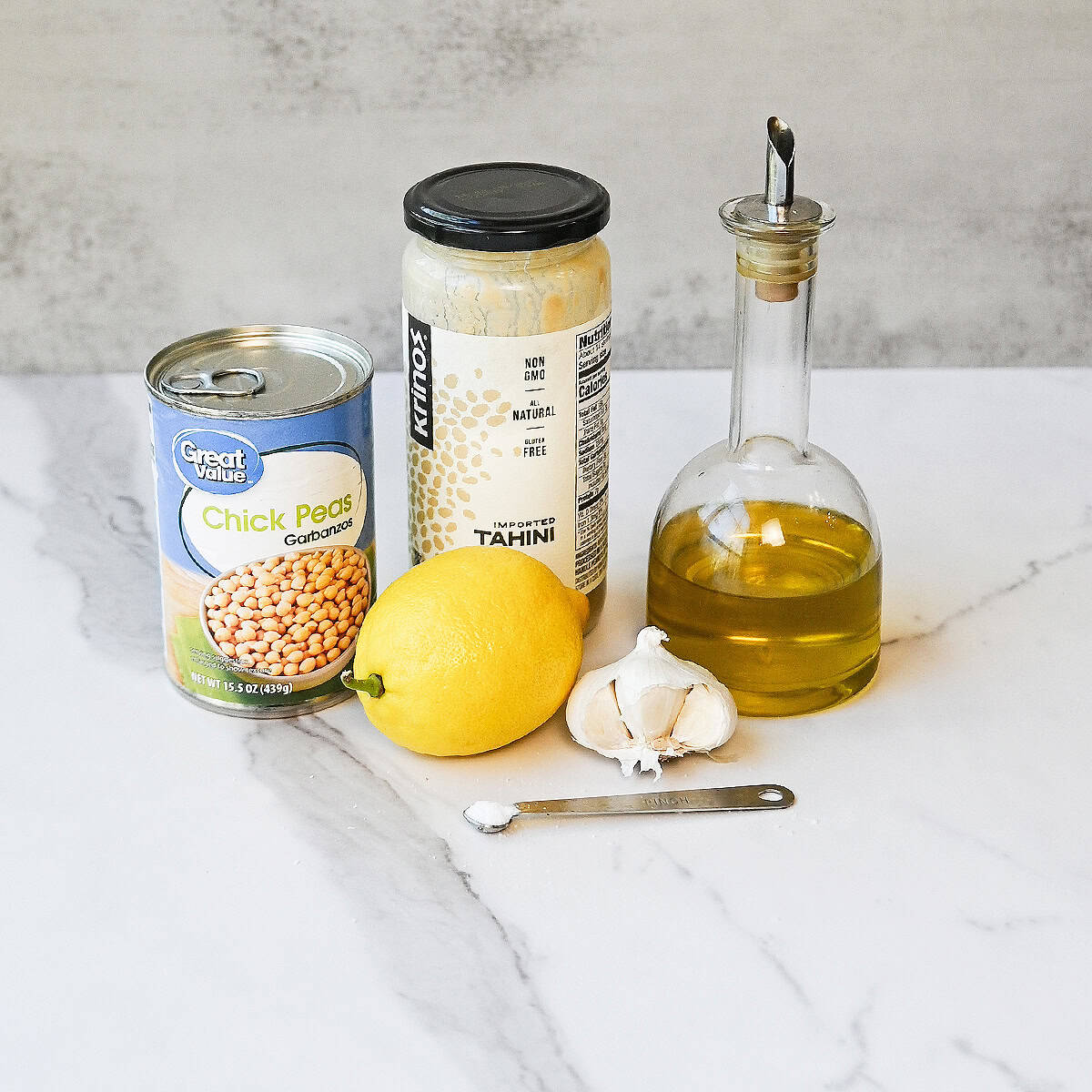 Ingredients for easy homemade hummus including chickpeas, tahini, lemon, garlic, olive oil, and seasonings arranged on a counter.